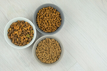 Variety of dry food for cats and dogs in ceramic bowls on a white wooden background. Copy space.