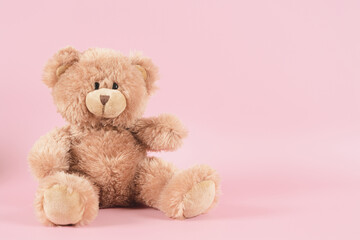 Brown teddy bear sitting on pastel pink background. Front view