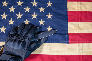 tactical gloves holding tactical knife on tea stained American flag - obrazy, fototapety, plakaty