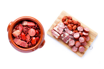 Brazilian feijoada, traditional food from Brazil, in ceramic bowl and ingredients on cutting board, isolated on white background