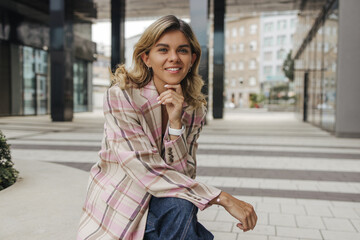 Fototapeta premium Pretty young caucasian woman smiling looking at camera sitting outside office on break. Blonde wears shirt and jeans. Concept of leisure, recreation