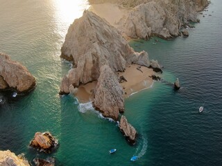Aerial of stone arch and rocky cliffs and boats in Cabo San Lucas, Mexico at sunset