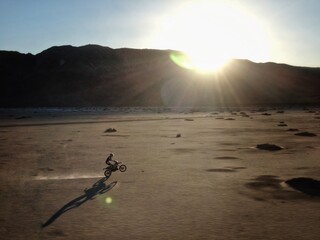 Dirt Biker doing wheelie across dry lakebed at sunset - obrazy, fototapety, plakaty