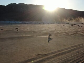 Dirt biker wheelie across dry lakebed in southern California desert at sunset