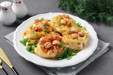 Tagliatelle pasta with turkey, vegetables and tomato sauce on a white plate on dark gray background