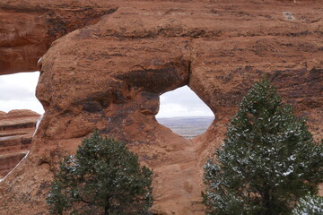 Snow covered pine trees and red sandstone arch in Arches National Park in Utah