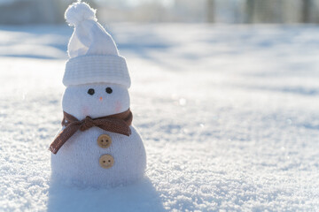 Figure of little cute snowman in a knitted hat and scarf on on snowy field in a sunny winter day. Concept for winter site head mockupcard or christmas card.