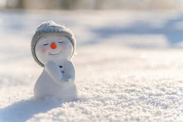 Figure of little cute snowman in a knitted hat and scarf on on snowy field in a sunny winter day....