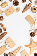Christmas frame background. Top view of brown gift boxes, accessories for handmade presents in green, golden and red, wooden decorations, pinecones, tags on white table, copy space, selective focus