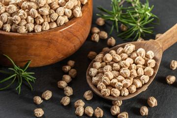 Dried raw chickpeas in wooden spoon and in wooden bowl, on a black background, closeup. Organic food. Legumes. Top view food. 