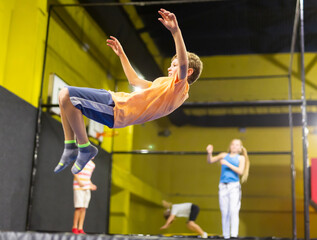 Fototapeta premium Happy active emotional preteen boy bouncing on trampoline while having fun in indoor amusement park..