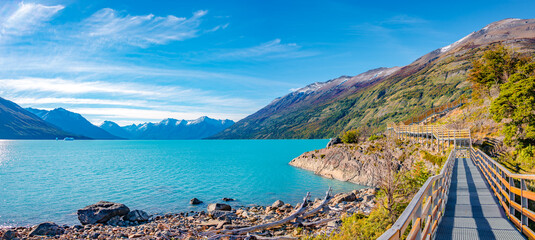 Panoramic view over blue sky and turquoise water glacial lagoon near Perito Moreno glacier in Patagonia with a modern metal walking path for tourists, South America, Argentina, in Autumn colors