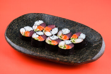 Set of maki sushi rolls with tuna, salmon, shrimp, cucumber and rice on red background.
