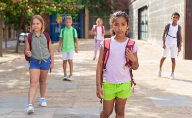 Fototapeta premium African-american girl with backpack standing outdoors. Other kids standing behind her.