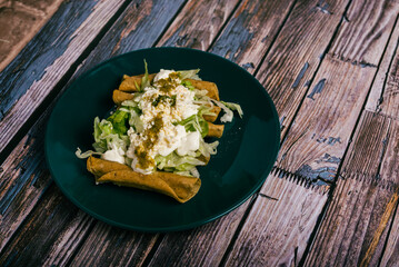 Tacos flauta with cheese, cream and lettuce on a wooden table. Mexican snacks.