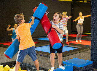 Expressive determined tween girl having funny wrestling by pugil sticks on battle beam with...