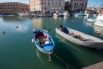 Fototapeta na wymiar Fishing boats on the water in Ortigia island with the cityscape of Syracuse in Sicily, Italy