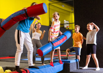 Expressive tween boy having fun on battle beam with his teenage older sisiter over foam pit in...