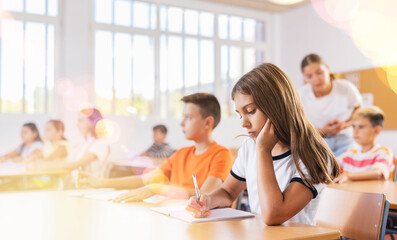 Obraz na płótnie Canvas Girl and boy sitting at desk in classroom with their classmates, listening to teacher explaining lesson subject.