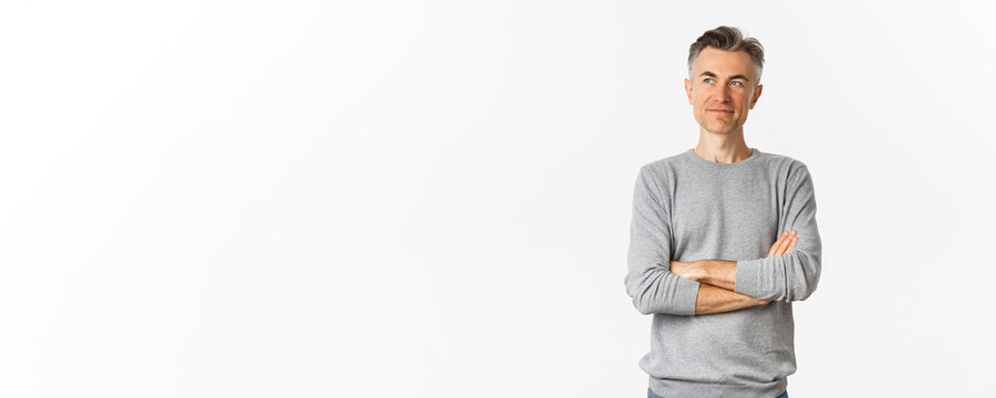 Portrait Of Confident Middle-aged Man Standing Over White Background, Cross Arms On Chest And Looking Pleased At Left Copy Space