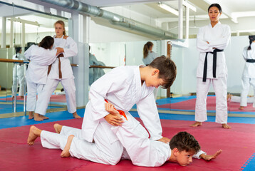 Fototapeta premium Two young boys training joint lock movement during group karate training. Their teacher standing behind and observing.