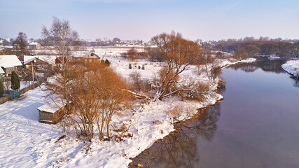 Winter river landscape, snow covered fields. Hoarfrost on trees, plants. Frosty evening. Sunny cloudy Misty weather. Cold season. Calm nature scene. Village - 555258899