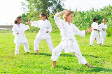 Naklejka na ściany i meble Schoolgirl eight years old in kimono with white belt exercising karate at summer park