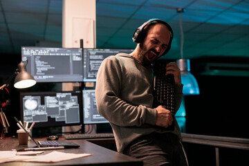 Male software engineer playing guitar with keyboard, writing code with cloud computing and...