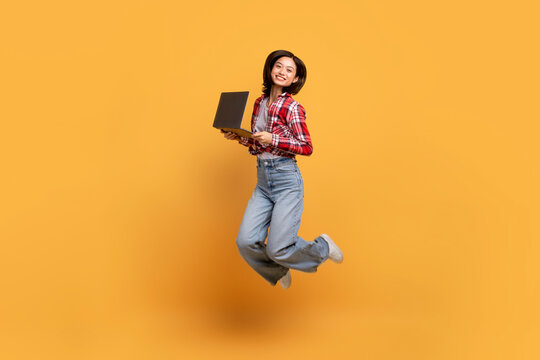 Full Body Length Of Happy Asian Lady Jumping And Holding Pc Laptop, Searching Discounts And Sales, Yellow Background