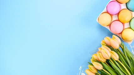 Spring flat lay with fresh yellow tulips colorful eggs on blue background. Easter, Mother day, birthday or Anniversary with copy-space. Sweet rainbow color Easter eggs, small pastel colors.