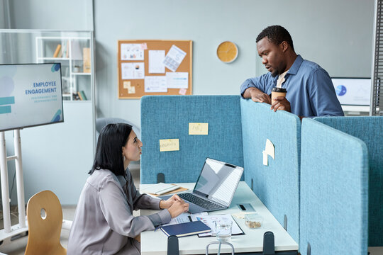 Side view at two young colleagues talking over cubicle wall in office, copy space