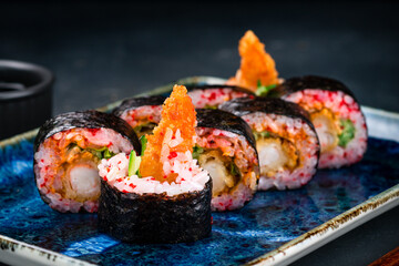 Maki sushi rolls with shrimp tempura, cream cheese, lettuce, cucumber and red flying fish caviar, closeup.