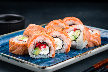 Japanese cuisine set of sushi rolls with seared salmon, cream cheese, avocado, rice, nori, red flying fish caviar and soy sauce.