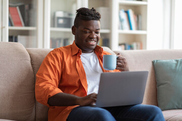 Relaxed black guy watching movie and drinking tea at home