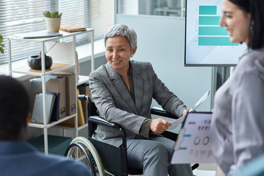 Portrait of smiling senior businesswoman using wheelchair in team meeting