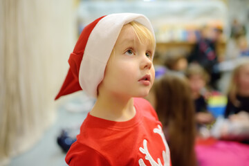 A cute toddler boy dressed in a sweater with a deer and a red Santa's hat looks fascinated