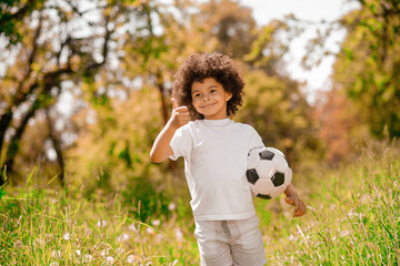 Curly-haired boy in white sportswear with a football