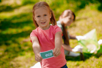 Blonde girl with eco symbol and her mom gathering garbage in the park