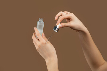 Cropped view of young lady applying regenerating anti-aging serum onto her hands over brown studio background