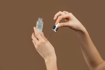 Cropped view of young lady applying regenerating anti-aging serum onto her hands over brown studio...