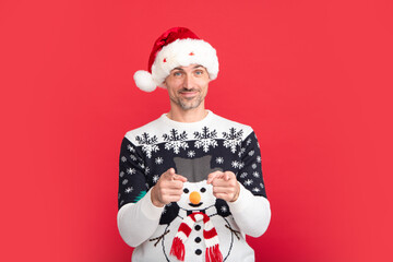 Handsome man in a winter sweater and Santa hat on studio red background.