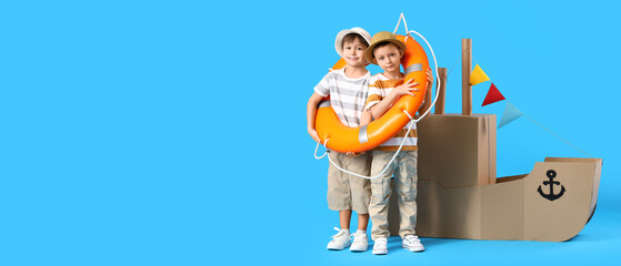 Little boys playing with cardboard ship on light blue background with space for text