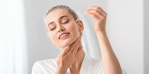 Beautiful young woman applying cosmetic oil on her skin in bathroom
