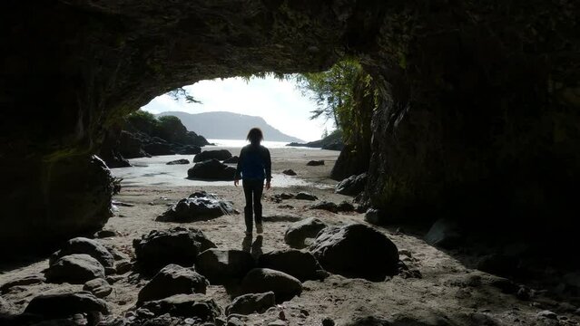 Woman Walking on in Cave on Beach with Pacific Ocean Coast View. Sunny Sky. San Josef Bay, Cape Scott Provincial Park, Northern Vancouver Island, BC, Canada. Canadian Nature Background. Cinematic 4k