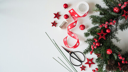 Christmas wreath door made natural christmas tree branches decorated with red berries,stars,cones,scissors and ribbon lie white table,top view,copy space.Concept for making Christmas wreath for home © Komchatnykh Tetiana