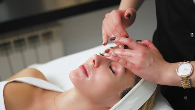 attractive Caucasian woman relaxing and having a facial massage in a spa salon, medium closeup skincare concept. High quality 4k footage