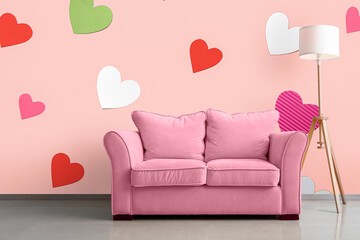 Pink sofa with lamp near pink wall with printed colorful hearts in room