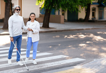 Young woman helping senior blind man to cross road in city