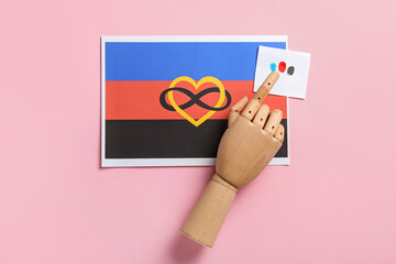 Wooden hand with paper sheet and polyamory flag on pink background