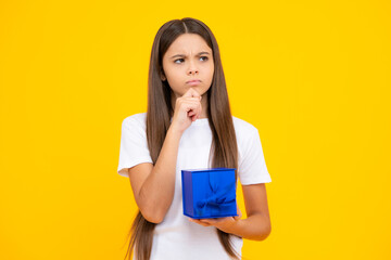 Child with gift present box on isolated yellow background. Presents for birthday, Valentines day, New Year or Christmas. Thinking face, thoughtful emotions of teenager girl.